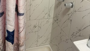 Un bagno con piastrelle in marmo, una doccia con porta in vetro e un lavandino bianco.
