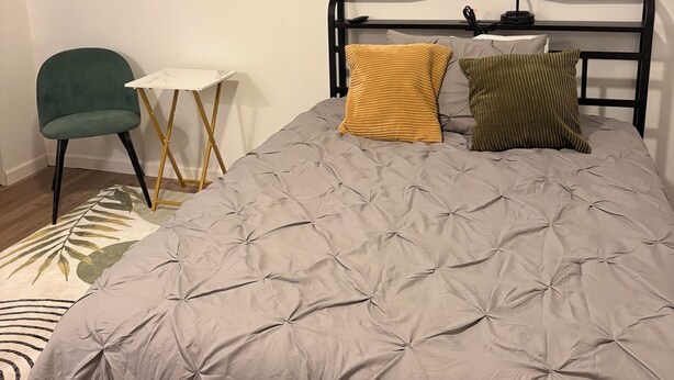 Un letto con una coperta grigia, un comodino, una lampada e una sedia.