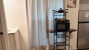 Una cucina con pavimento in legno, un frigorifero, un forno a microonde e uno scaffale con elettrodomestici.