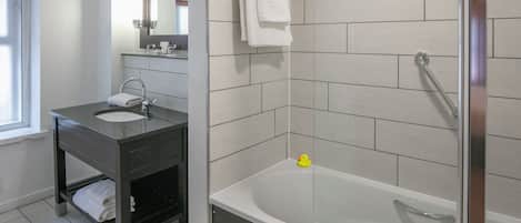 A modern bathroom with a dark vanity, a white sink, a mirror, and a bathtub with a rubber duck.