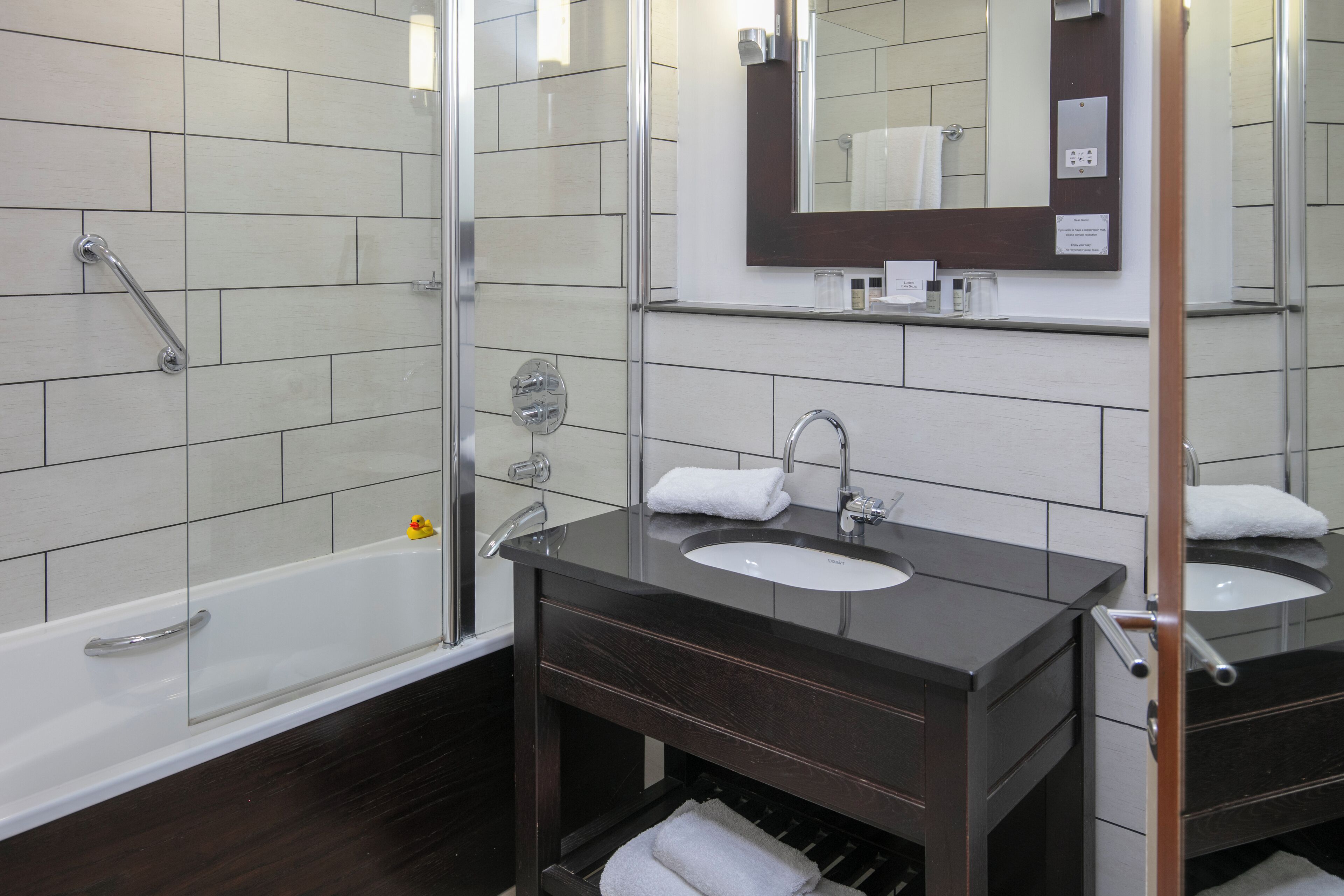 A modern bathroom with a glass shower enclosure, a vanity with two sinks, and a mirror above the vanity.