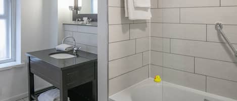 A modern bathroom with a dark vanity, a white sink, a mirror, and a bathtub.
