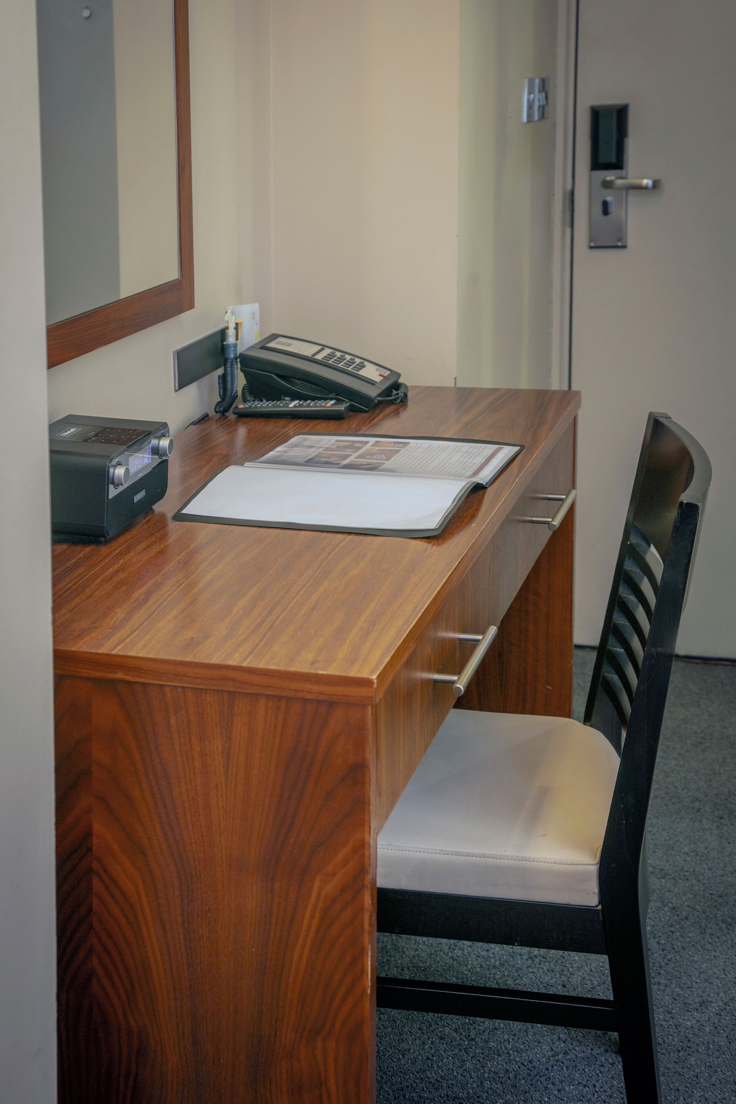 Escritorio de madera con teléfono, máquina de fax y un documento. Silla con asiento acolchado y estructura de metal negro.