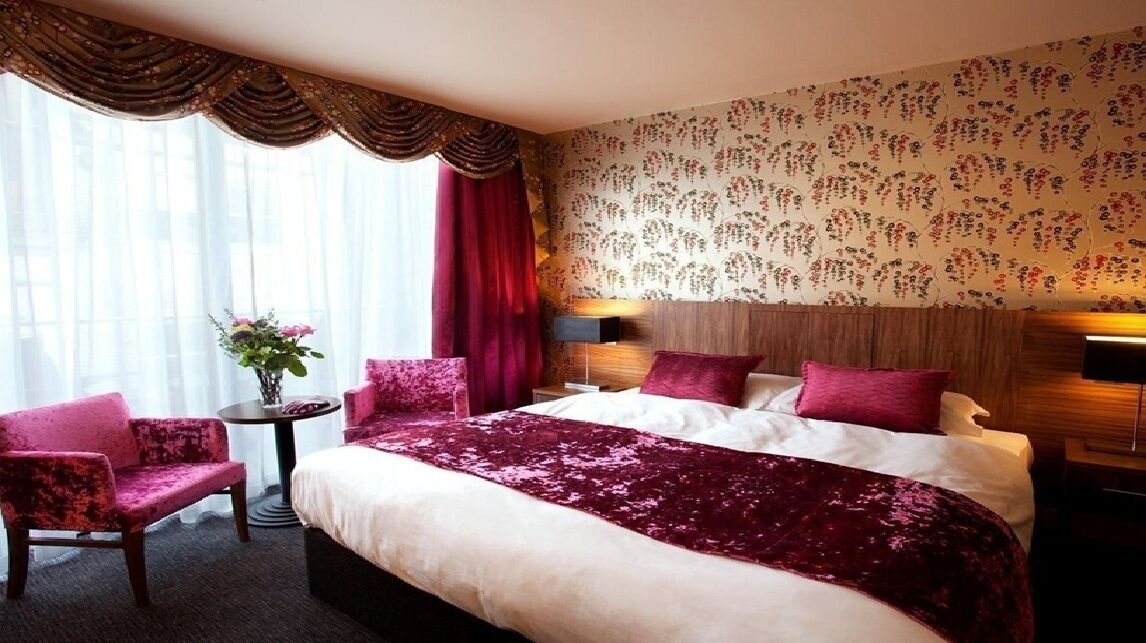 Una habitación de hotel con una cama grande, dos mesitas de noche, una pequeña mesa redonda y dos sillas.