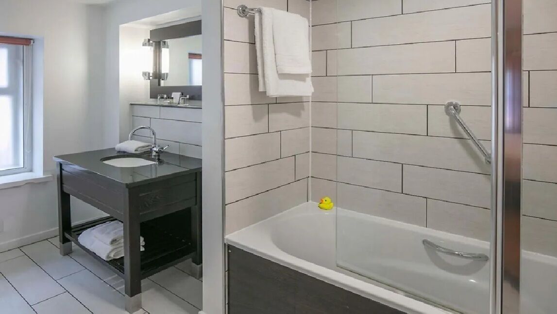 Une salle de bain moderne avec un meuble-lavabo foncé, un lavabo blanc, un miroir et une baignoire.