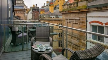 Un balcón con mobiliario de mimbre y una mesa, con vista a un paisaje urbano con edificios históricos.