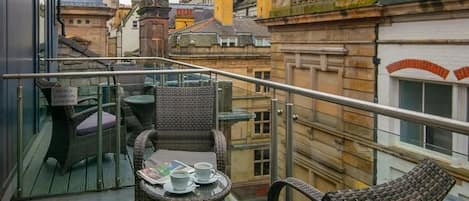 A balcony with wicker furniture and a table, overlooking a cityscape with historic buildings.