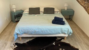Une chambre à coucher avec un lit, deux tables de chevet, une lampe, une couverture et une grande peau de vache sur le sol.