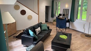 Un salon moderne avec un canapé, une table basse et un téléviseur. Un escalier mène à un autre niveau, et il y a une fenêtre avec des rideaux.
