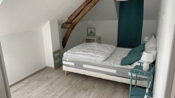 A bedroom with a sloped ceiling, a bed with white bedding, a teal nightstand, a small bedside table with a lamp, and a sign on the wall.