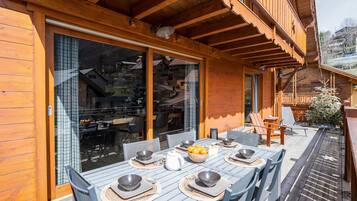Une terrasse en bois avec une table à manger pour quatre personnes, entourée de chaises.
