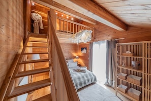 Ein Holzblockhaus-Interieur mit Treppe, einem Bett, einem Regal mit Aufbewahrungsboxen und einem Fenster mit Vorhängen.