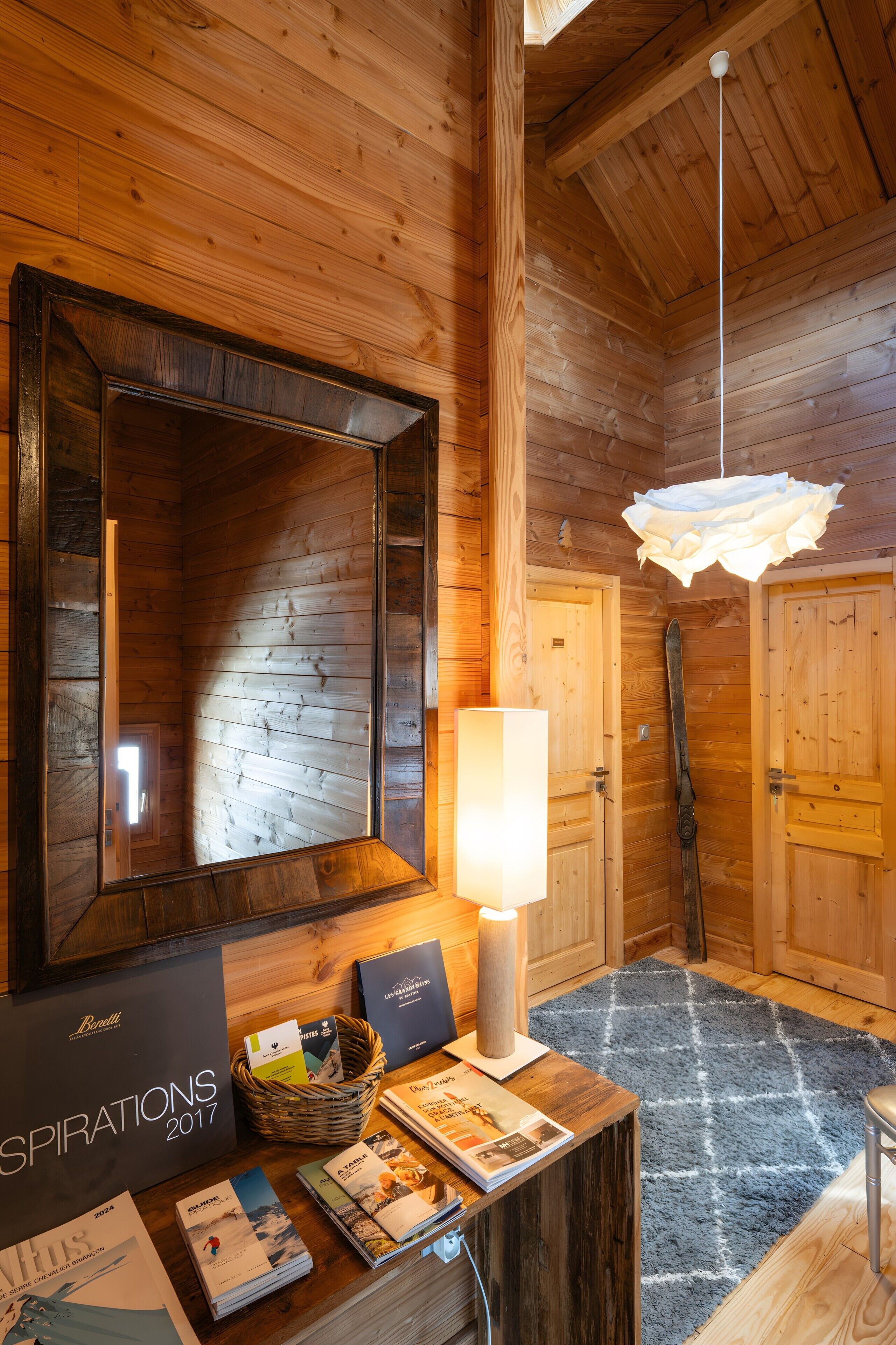 Un intérieur en bois agrémenté d’un grand miroir, d’un luminaire suspendu et d’une table sur laquelle sont disposées des brochures et une lampe.