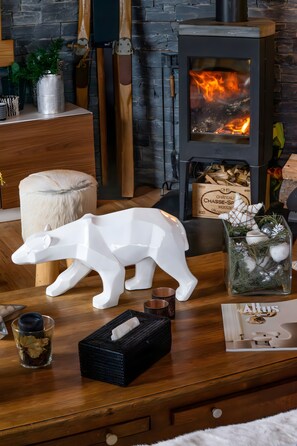 A cozy room with a wood-burning stove, a white polar bear sculpture, a wicker basket, and a glass container with leaves. - Guest Room 'Chambre Izoard at the Datcha' with Mountain View, Private Terrace and Wi-Fi (Briançon)