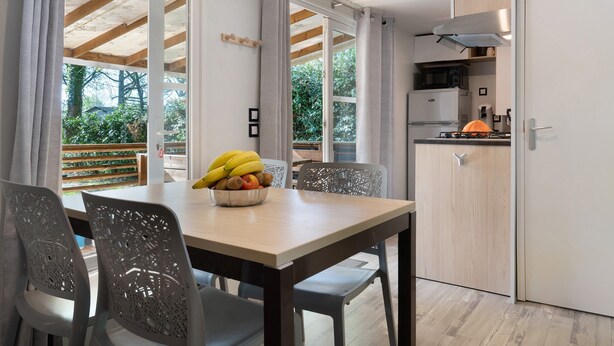 A modern kitchen with a dining area, wooden beams, and a view of greenery.