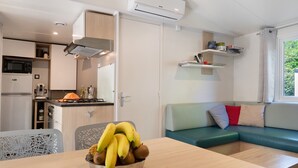 A compact kitchen with a microwave, stove, and cabinets, a dining table with a bowl of fruit, and a green sofa with cushions.