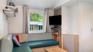 A room with a sofa, a table, a TV, and a window with curtains.