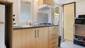 A compact kitchen with wooden cabinets, a gas stove, a microwave, and a window with blinds.