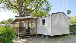 A single-story mobile home with a porch, a satellite dish, and a small deck.