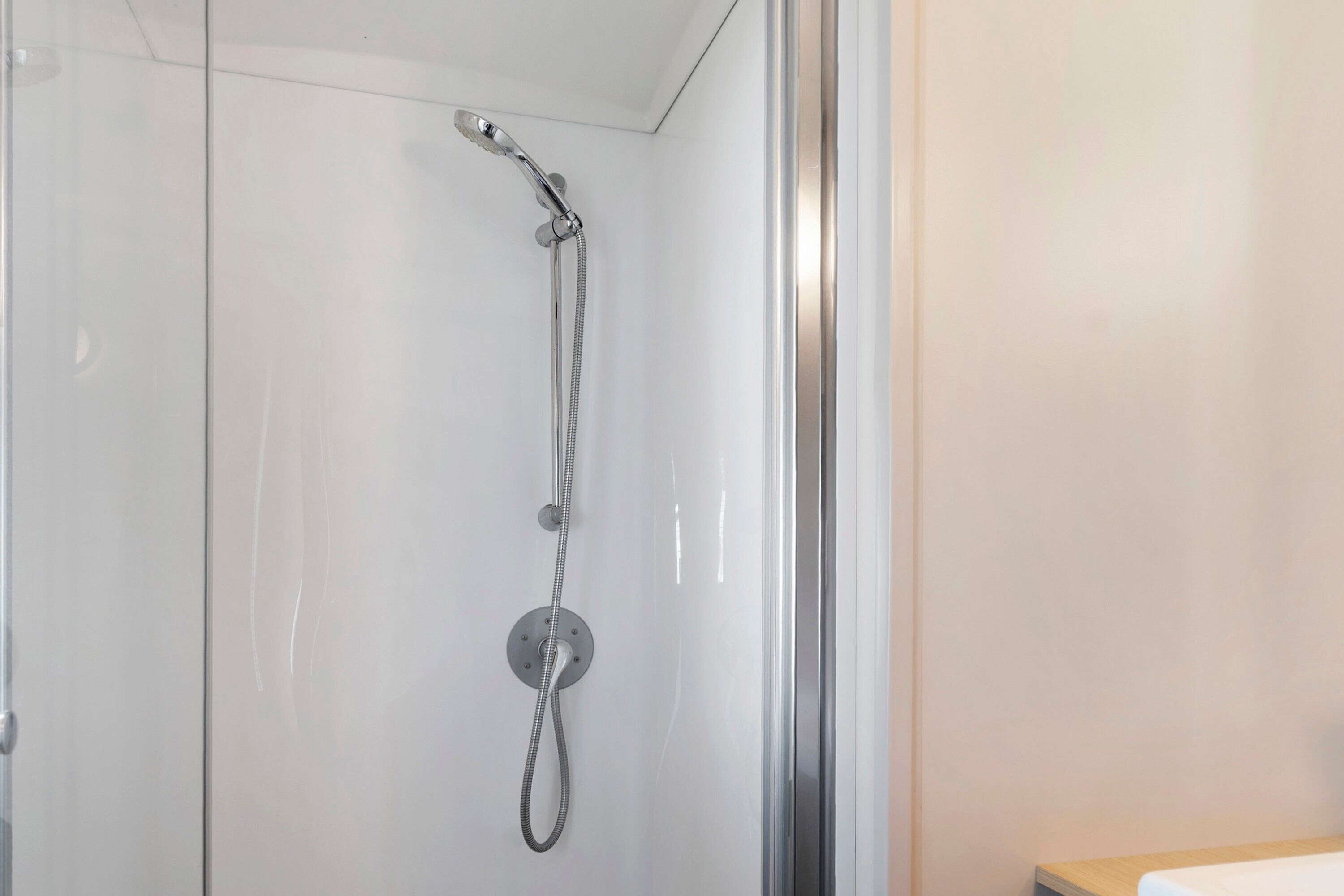 Ein modernes Badezimmer mit Duschkabine aus Glas, einer sichtbaren Duschbrause und einer Holzauskleidung.