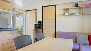 A compact kitchen with a stove, microwave, and open shelving; a dining table with chairs; and a sofa with cushions.