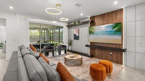 Un salon moderne avec un canapé gris, des poufs orange et un grand téléviseur fixé au mur.