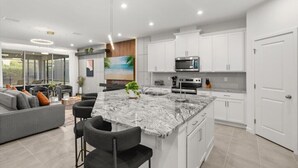 Une cuisine moderne avec des meubles blancs, un îlot en granit et un grand îlot doté de tabourets de bar.