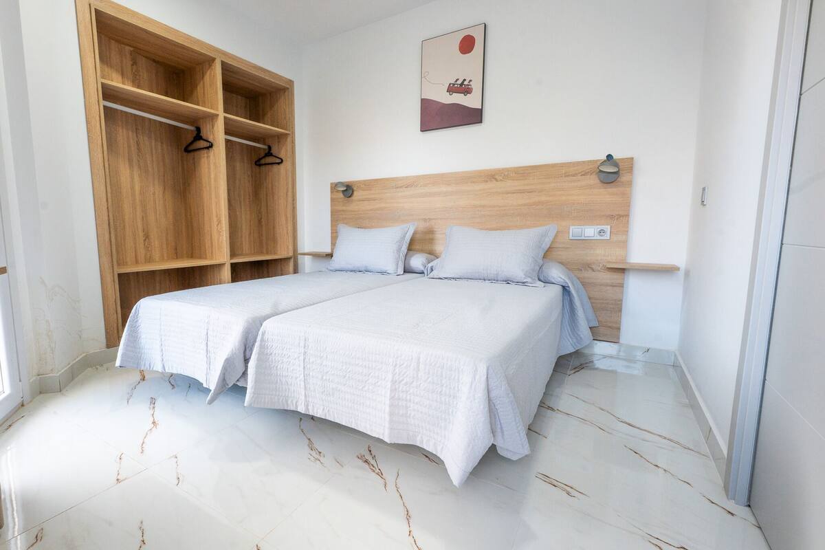 Une chambre avec deux lits, une tête de lit en bois et une armoire dotée de plusieurs étagères.