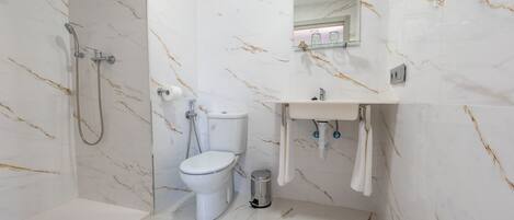 Baño con inodoro, ducha y lavamanos, todo en un espacio compacto con paredes de mármol.