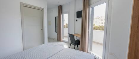 A hotel room with a bed, a desk, and a chair. There is a sliding door leading to a balcony.