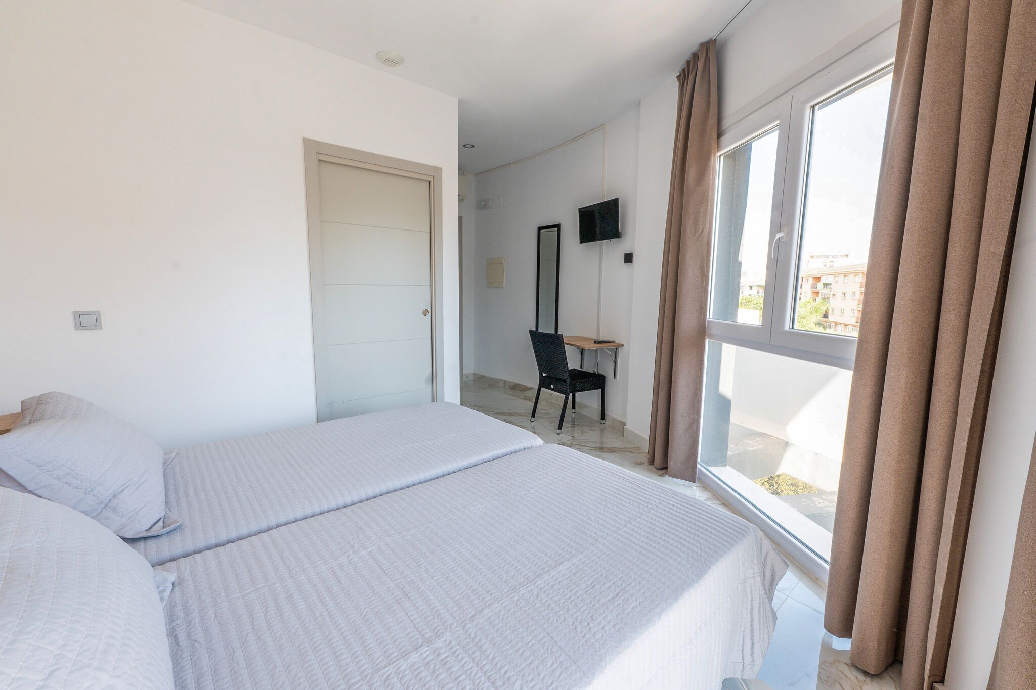 A hotel room with a bed, a desk, a chair, a TV, and a window with curtains.