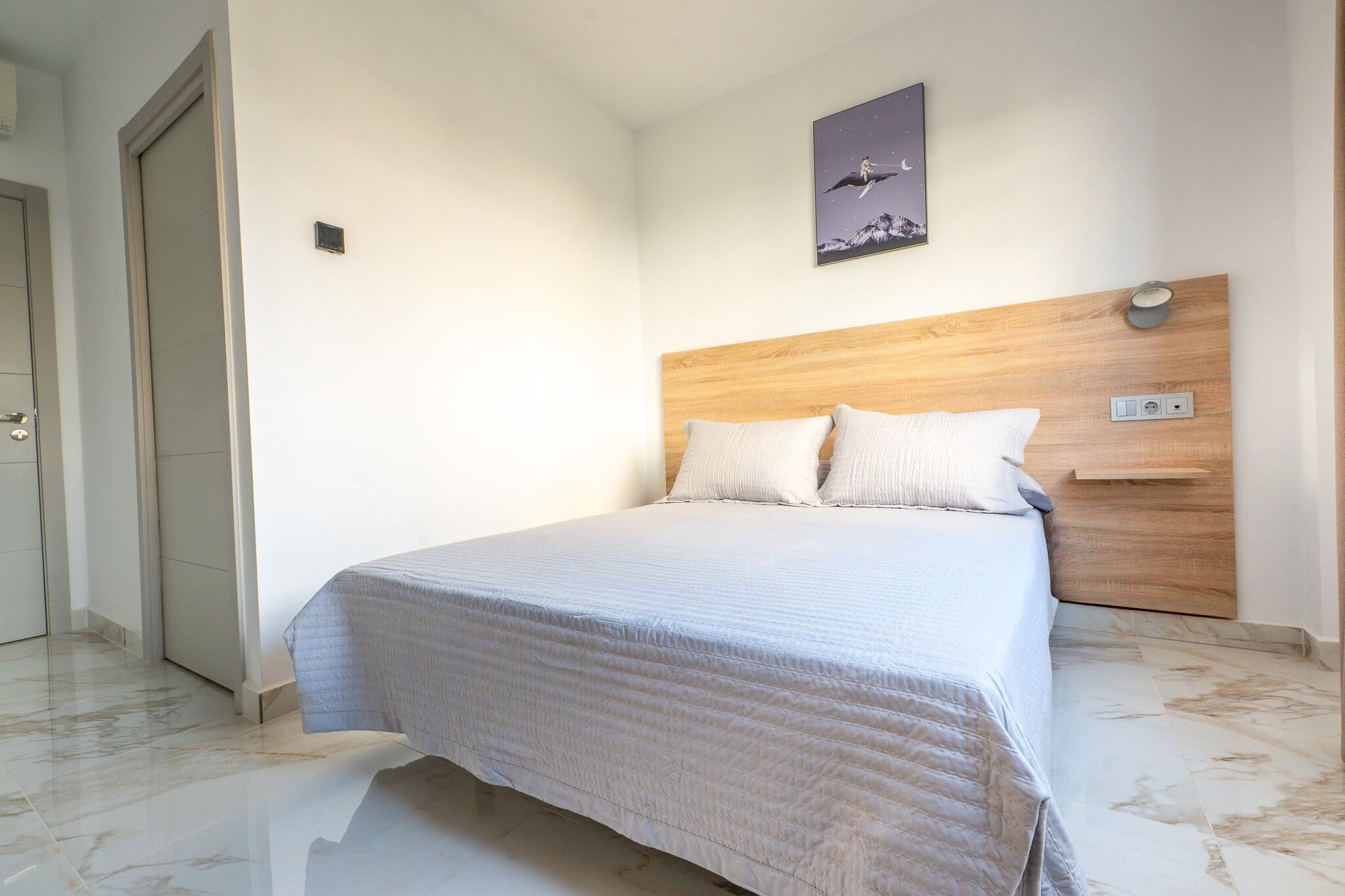 Een slaapkamer met een bed, een houten hoofdbord, een nachtkastje en een wandlamp.
