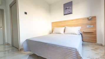 Quarto com cama, cabeceira de madeira, mesa de cabeceira e luminária na parede.