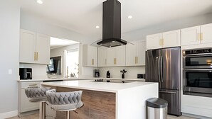 A modern kitchen with white cabinets, a stainless steel refrigerator, and a central island with bar stools. - 6BD/4BA Windsor Luxury Villa | Game Room & Pool (Kissimmee)