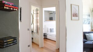 Un couloir mène à un salon où se trouvent un canapé et un tableau encadré accroché au mur.