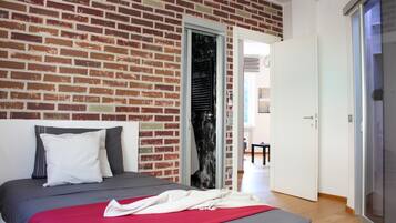Ein Schlafzimmer mit Backsteinwand, einem Bett mit grauer Bettwäsche, einem weißen Kopfkissen und einer roten Decke.