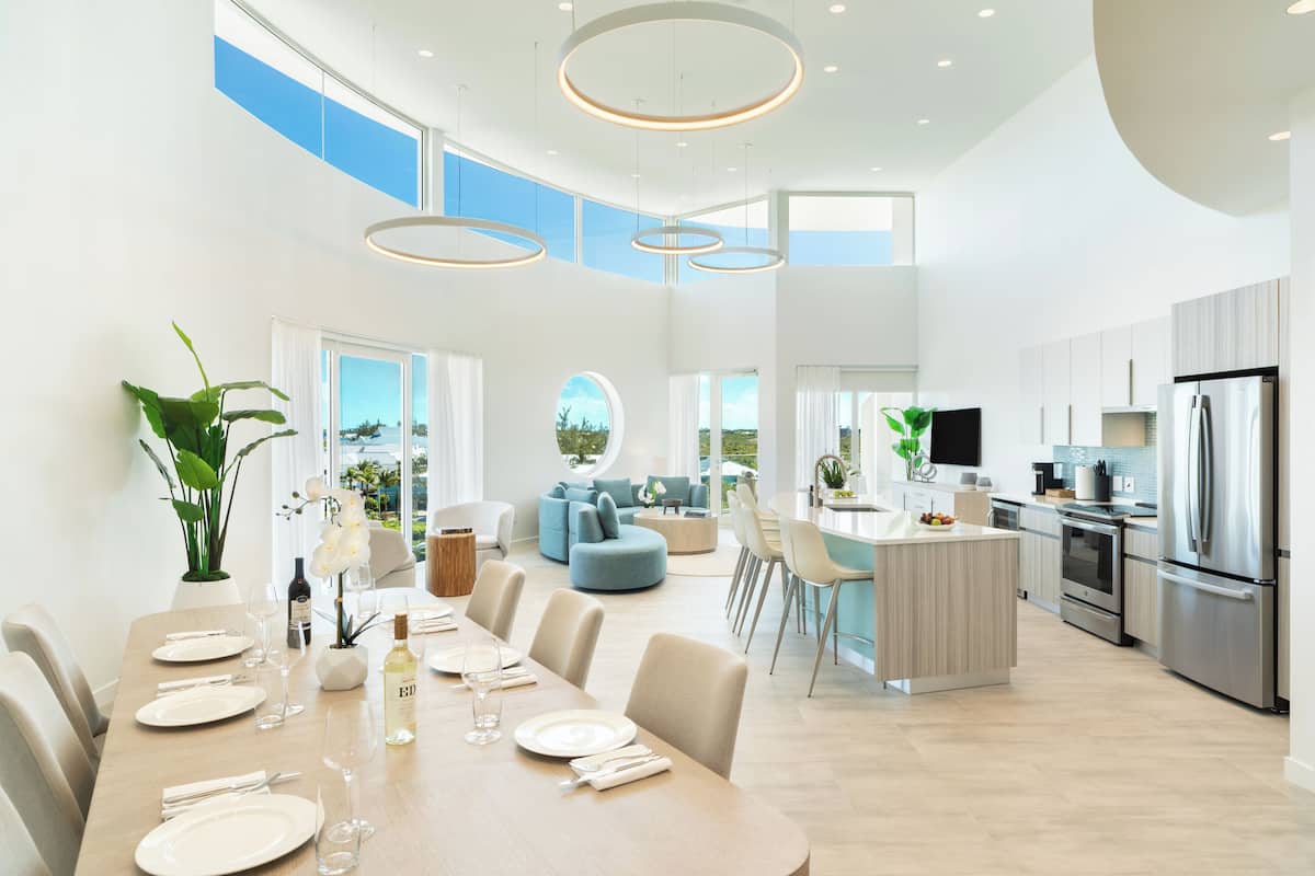 A spacious kitchen with modern appliances, a dining area with a long table set for a meal, and a living area with a sofa and a TV.
