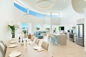 Een ruime keuken met moderne apparaten, een eetgedeelte met een lange tafel gedekt voor een maaltijd, en een woonruimte met een bank en een televisie.