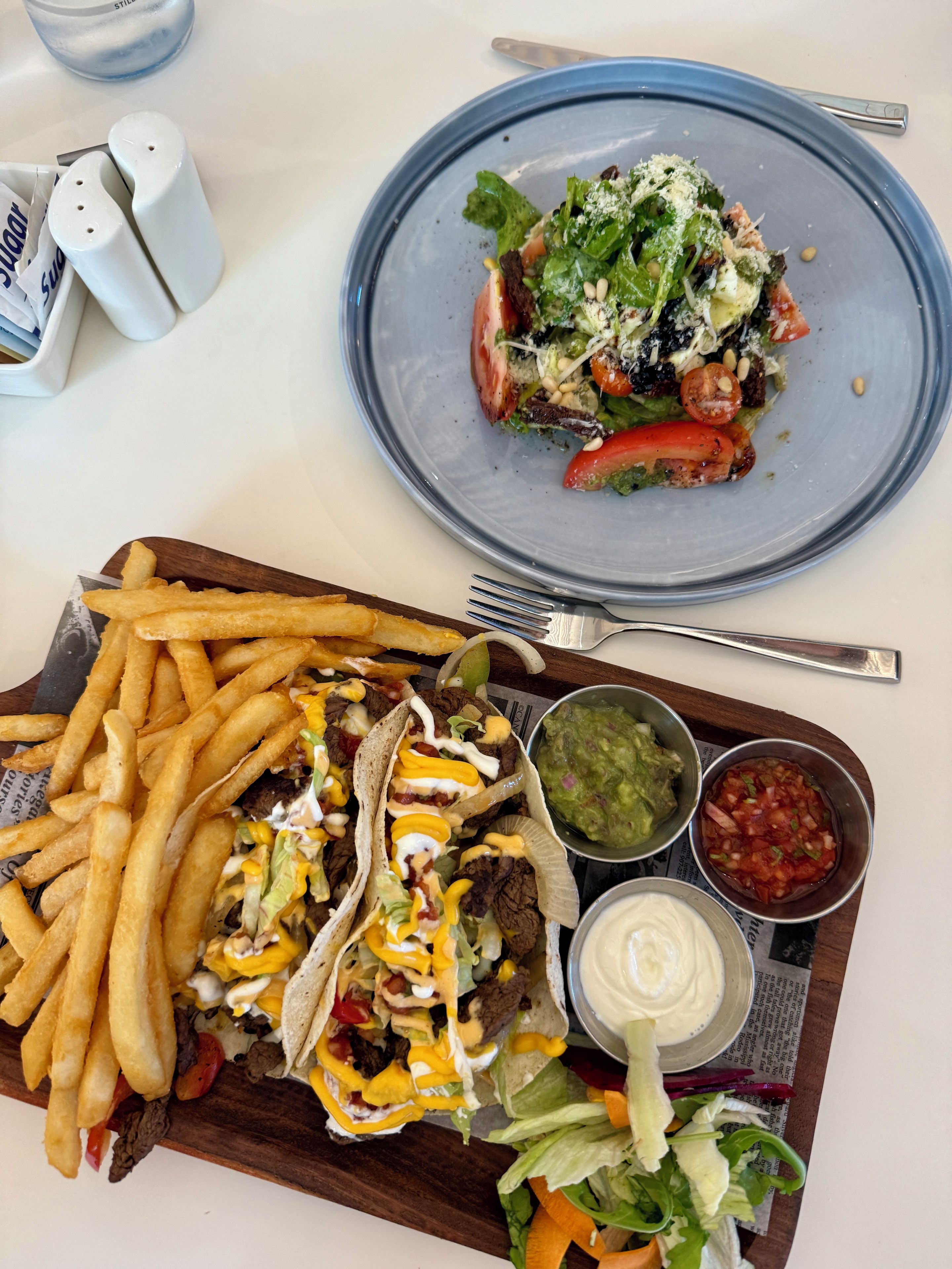 Eine Mahlzeit mit Pommes, Tacos und einem Salat auf einer Holzbrett.