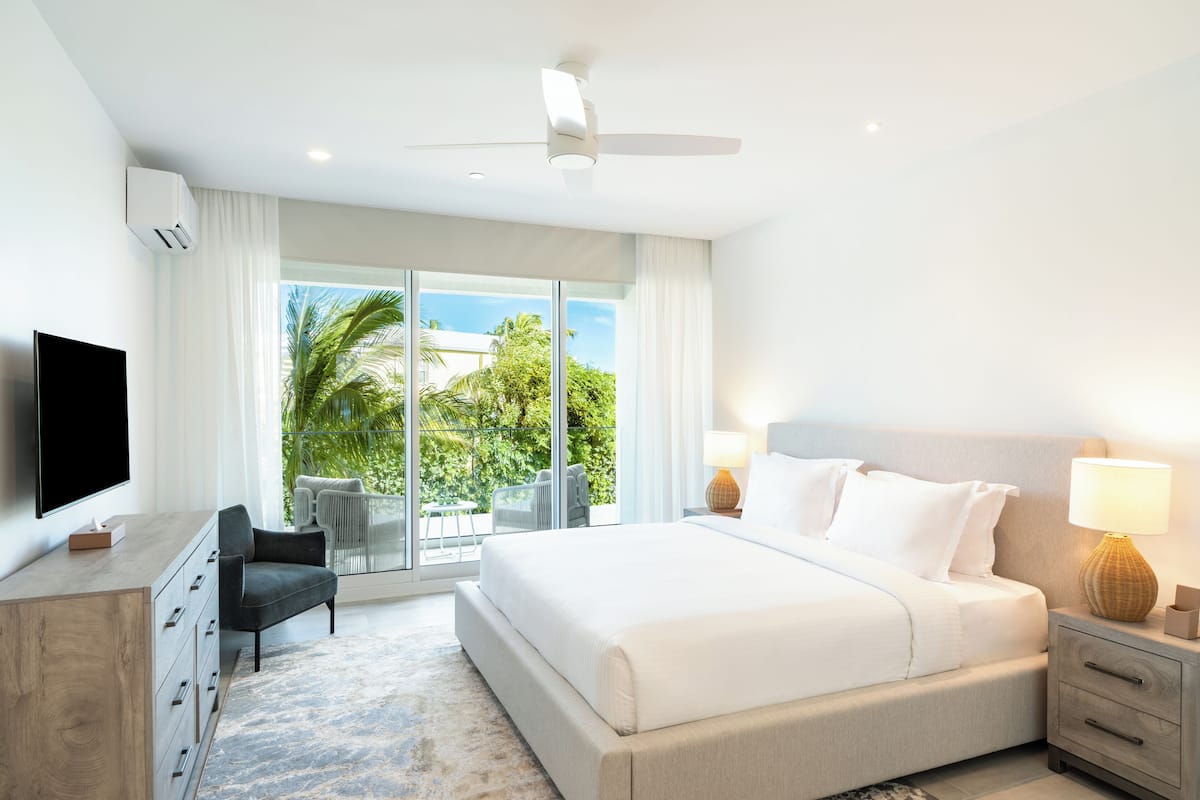 A modern hotel room with a large bed, a flat-screen TV, a desk, and a view of the outdoors.