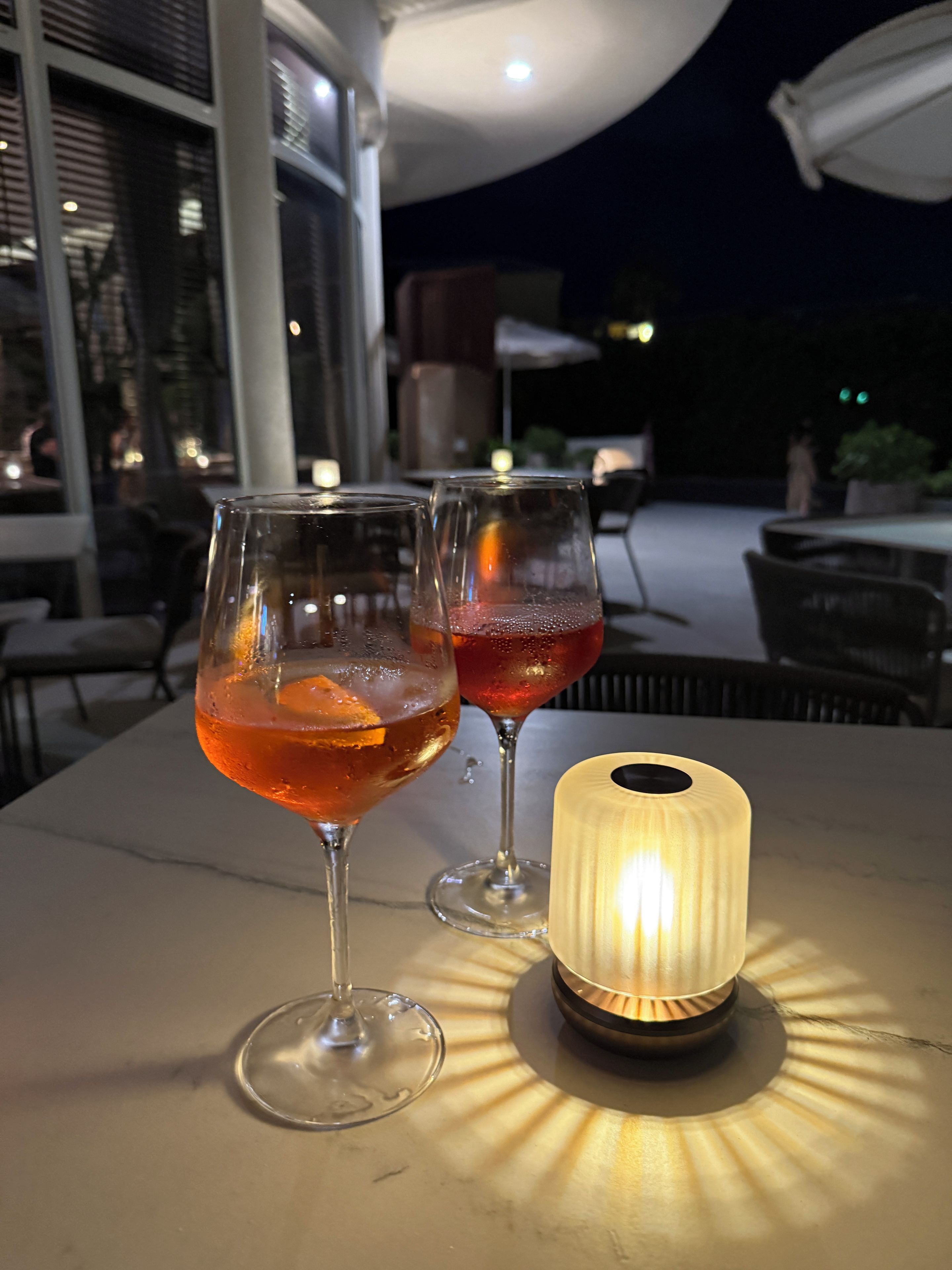 Two glasses of red beverage on a table with a lit candle.