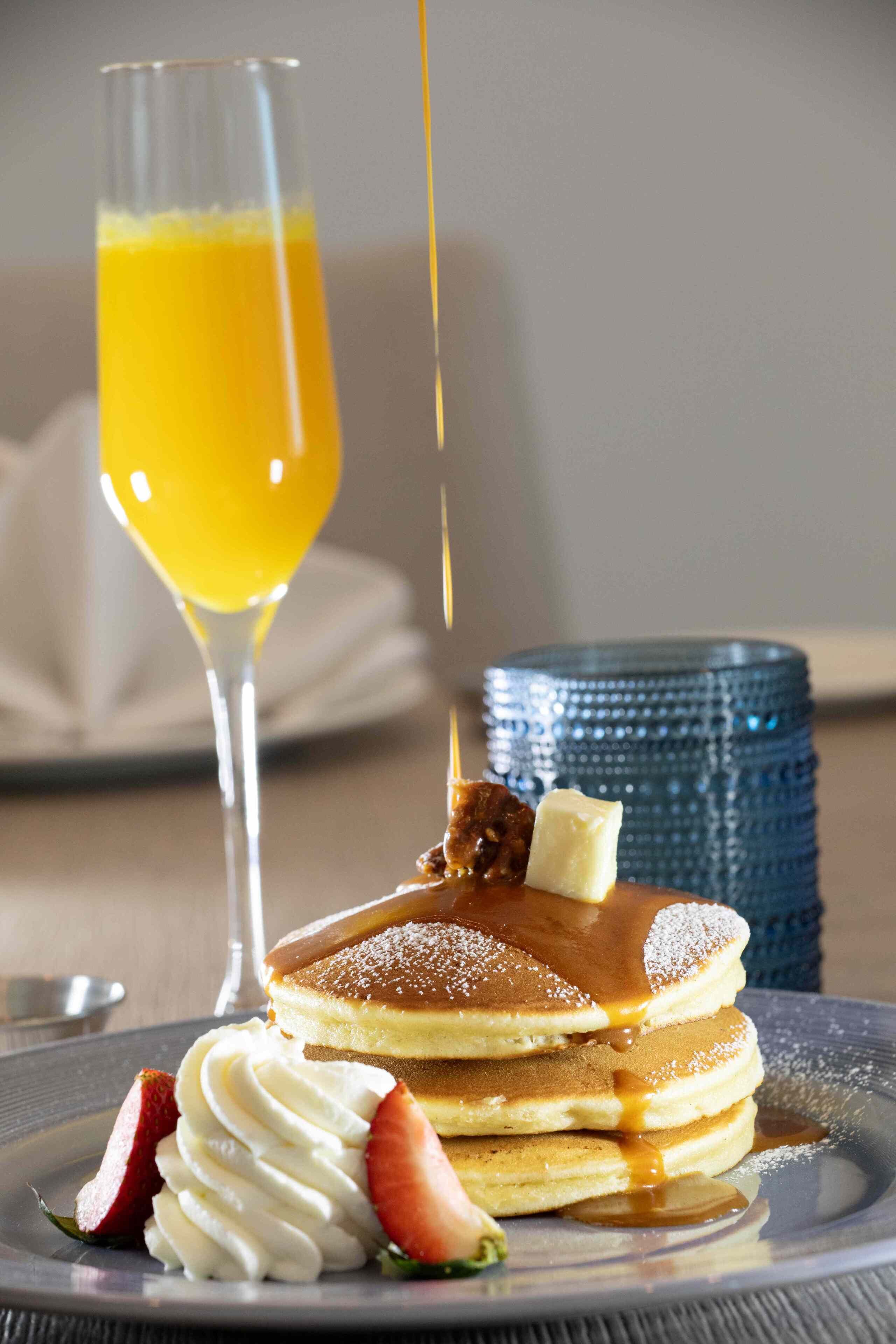 Ein Stapel Pfannkuchen mit Sirup, Schlagsahne und Obst auf einem Teller.