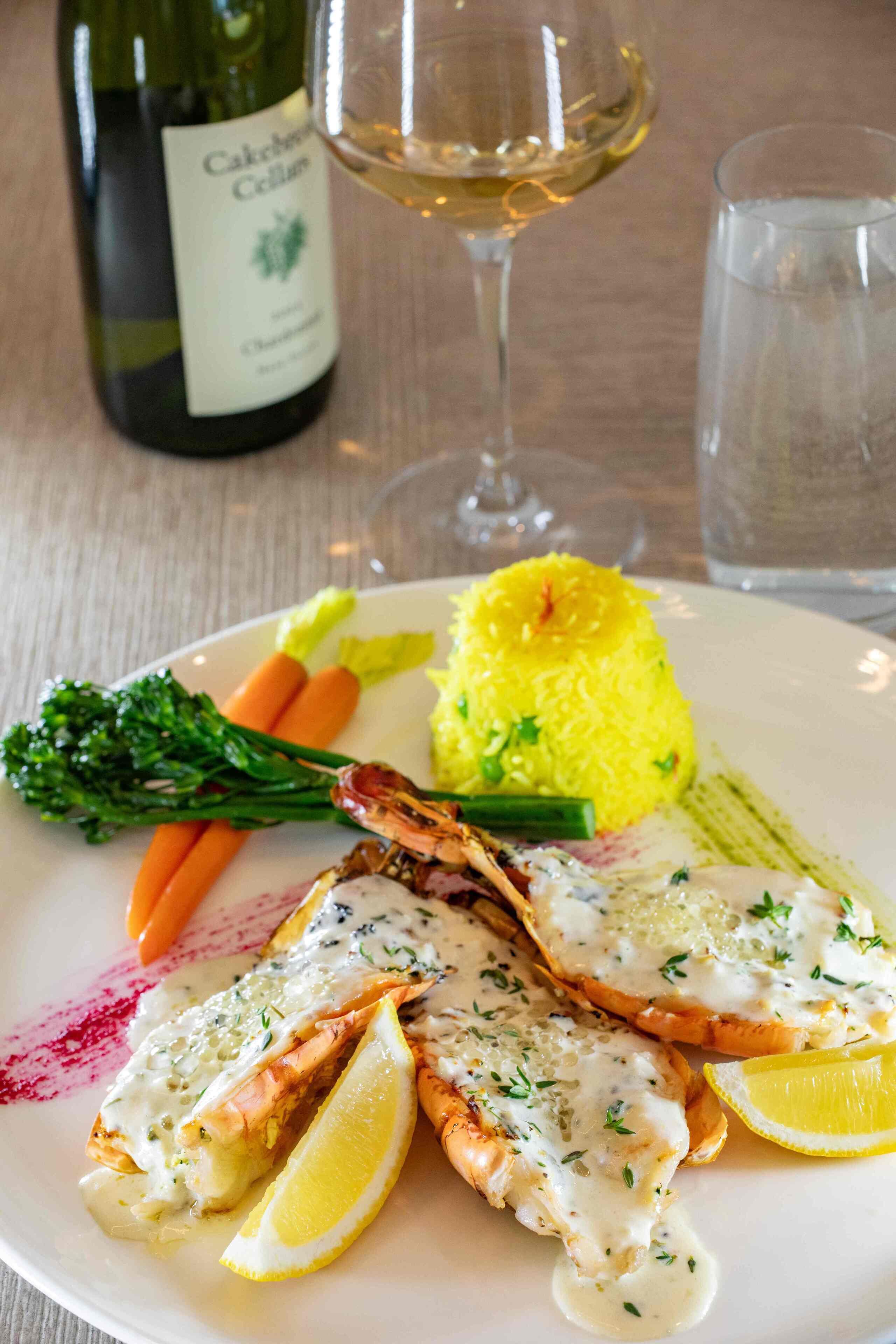 A plate of food with salmon, lemon, and vegetables, and a bottle of wine in the background.
