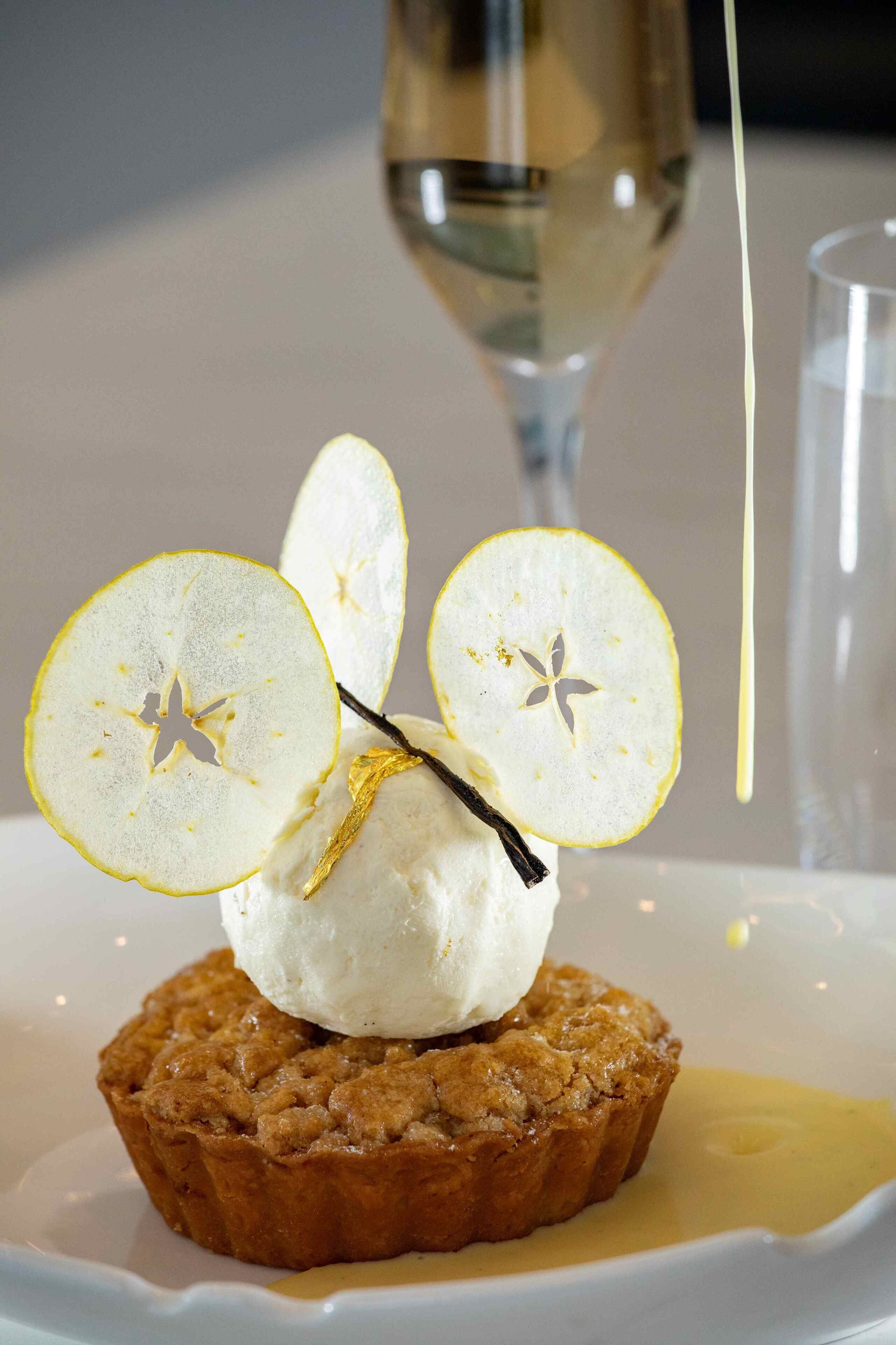 A dessert with a scoop of ice cream on top of a muffin, garnished with apple slices and a vanilla bean.