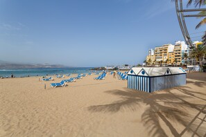 A beach with blue lounge chairs, a beach hut, and a building with balconies.