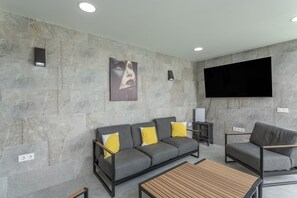 A modern living room with a grey sofa, yellow cushions, a wooden coffee table, and a flat-screen TV mounted on the wall.