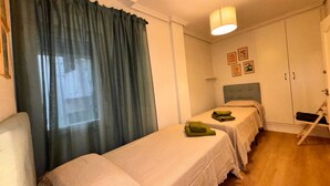 A room with two single beds, a chair, a wardrobe, and a window with curtains. - Rooms Carlos, next to Plaza Mayor (Madrid)