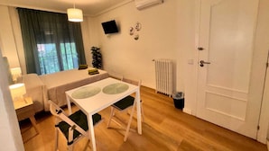 A small, well-lit room with a bed, a table with chairs, a radiator, and a door. - Rooms Carlos, next to Plaza Mayor (Madrid)