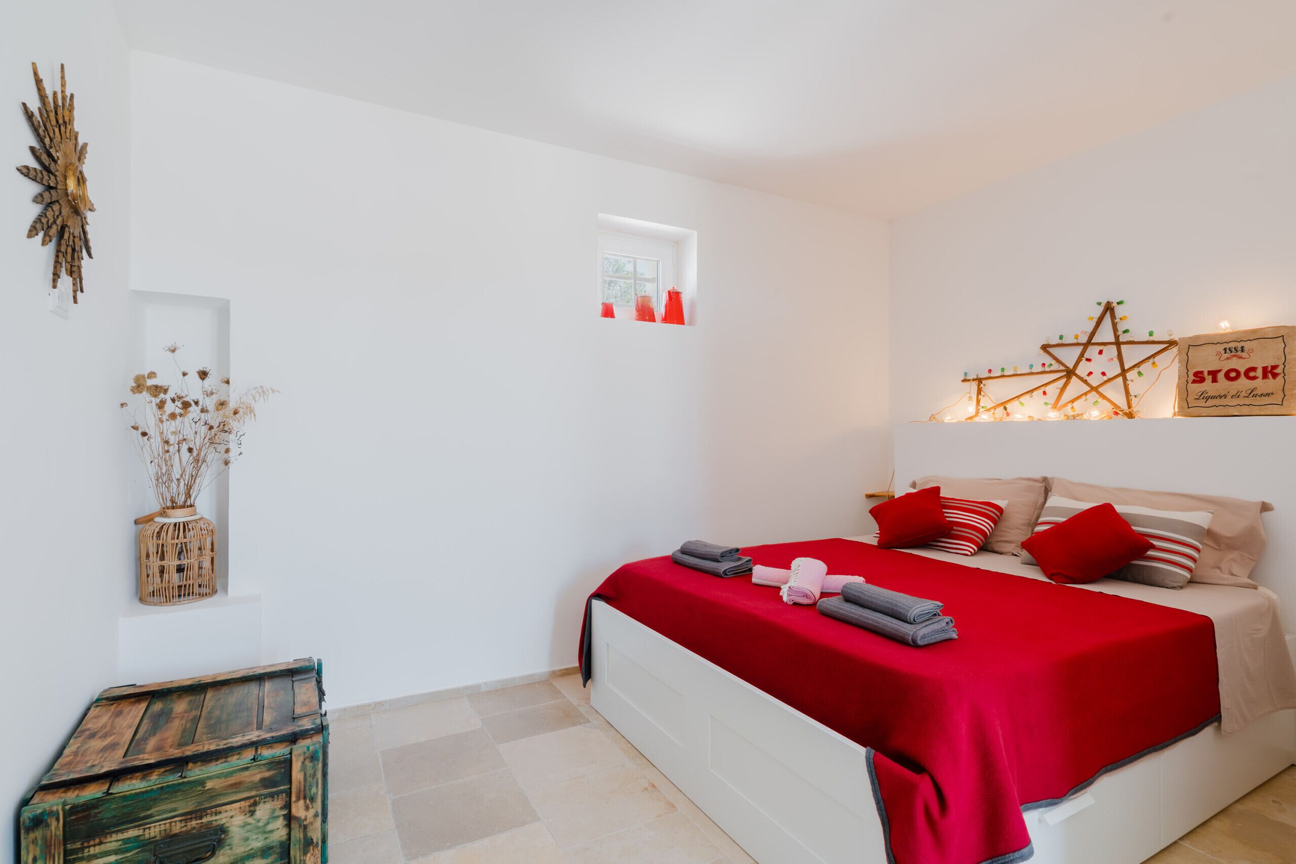 Een slaapkamer met een wit bed, rode beddengoed en een klein raam.