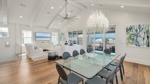 A spacious dining area with a glass table and modern chairs, a ceiling fan, and a large chandelier. - Grayton Gold|Easy Beach Access|Private Pool|Golf Cart (Santa Rosa Beach)